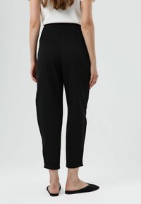 Zwarte, op maat gemaakte broek met een hoge taille, smalle pasvorm, subtiele plooien en cropped lengte. Gladde stof met een matte textuur.