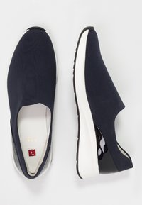 Marina slip-on skor med en texturerad ovandel, vit mellansula och glänsande svarta hälaccenter. Rundad tå och ingen synlig snörning.