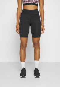 Czarne rowerowe spodenki o wysokim stanie wykonane z elastycznej tkaniny, z gładką fakturą i długością do kostek, połączone z czarnymi sneakerami i białymi skarpetkami.