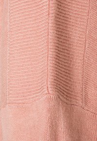 Gros plan sur un tissu tricoté rose doux avec des motifs côtelés verticaux et horizontaux et des lignes de couture visibles.
