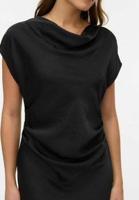 Černý vršek s volánem u výstřihu, krátké rukávy a hladká textura. Má volný střih se shromážděným detailem na boku.