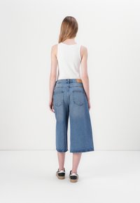 Denim culotter med en avslappet passform, rå kant og to baklommer. Kombinert med en hvit tanktopp og svarte sneakers.