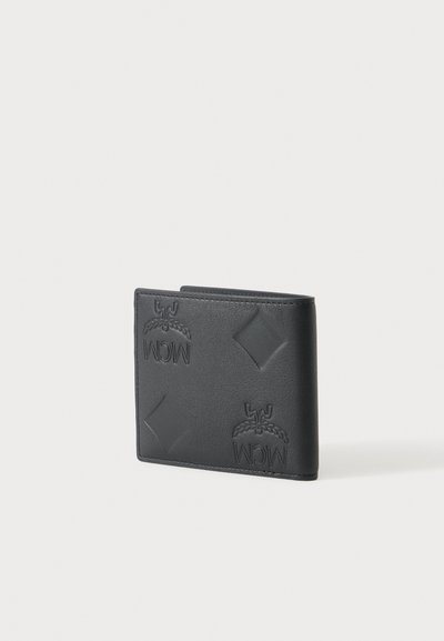 Portefeuille bifold en cuir noir embossé de formes losanges et de logos « MCM », posé sur une surface blanche.