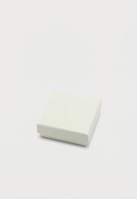 Μικρό κλειστό λευκό τετράγωνο κουτί με διακριτική υφή, τοποθετημένο σε απλή λευκή επιφάνεια.