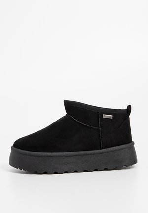 Bottine en daim noir avec semelle épaisse en caoutchouc et étiquette latérale, design sans lacets et languette au talon.