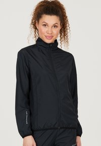 Sort letvægtsjakke med høj krave, fuld lynlås, elastiske manchetter og brandede detaljer på ærmerne. Glat stof med en tætsiddende design.