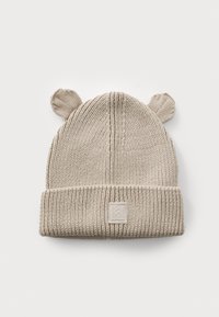 Bouton beige tricoté avec des oreilles d'ours, texture côtelée et revers replié. Présente un patch de marque monochromatique en forme carré sur le devant.