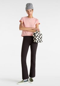 Roze T-shirt met korte mouwen met Vans-logo, zwarte flared broek, grijze gebreide beanie en zwart-wit geblokte tas. Groene slip-on schoenen.