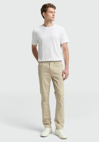 Beige Chinos mit geradem Schnitt, kombiniert mit einem schlichten weißen Kurzarm-T-Shirt und weißen Sneakers. Glatte Stoffoberfläche, legerer Stil.