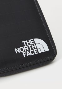 Juodas audinio piniginė su tinklelio tekstūra, siuvinėta briauna ir išraiškingu baltu "THE NORTH FACE" logotipu su mėnulio arkos dizainu.