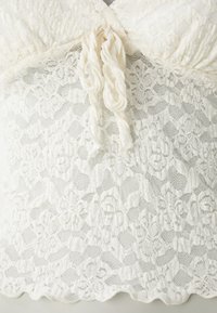 Hvit blonde topp med blomsterdesign, rynket halslinning og flettebånd detalj. Mykt stoff med bølget kant.