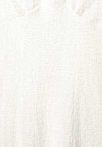 Tissu blanc texturé avec un motif en relief, apparence douce et légèrement duveteuse, présentant une couleur neutre et claire avec une surface uniforme.