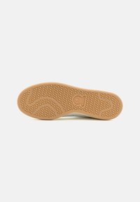 Podešev gumové tenisky v béžové barvě s texturovaným vzorem ve tvaru plástve a zakřiveným designem. Na patě je umístěno značkové logo.