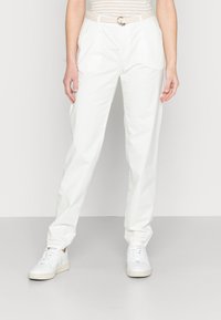 Pantalons en coton blanc avec une coupe décontractée, présentant une ceinture tressée et des poches latérales discrètes, associés à des baskets blanches.