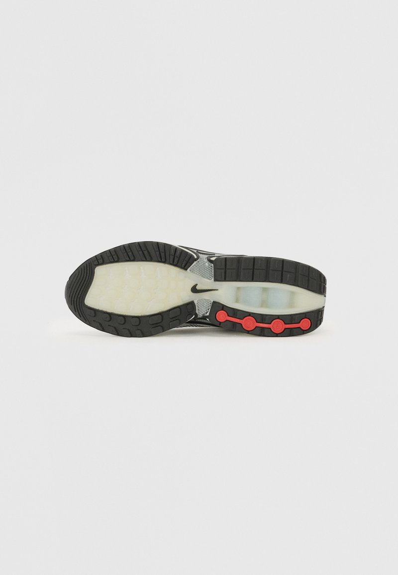 Semelle de chaussure de sport en noir et blanc avec une semelle intermédiaire translucide, une semelle extérieure en caoutchouc texturé, et des accents circulaires rouges sur le côté.