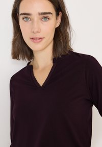 V-hals top in donkerpaars, gemaakt van een gladde stof. Heeft een subtiele kraag, lange mouwen en een getailleerde pasvorm.