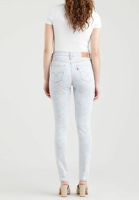Vaqueros skinny en azul claro con un patrón floral pastel, de talle alto con costuras decorativas, parche de cuero marrón y bolsillos traseros.