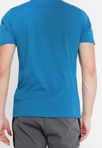 Camisa ajustada de manga corta en algodón azul brillante, con cuello redondo y textura suave, mostrada desde la parte de atrás sin logos visibles.