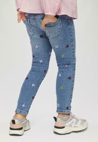 Denim teksad värviliste lillede ja liblikate tikandiga, kitsas lõige, pahklane pikkus, kombineeritud mitme tooni sportlike kingadega.