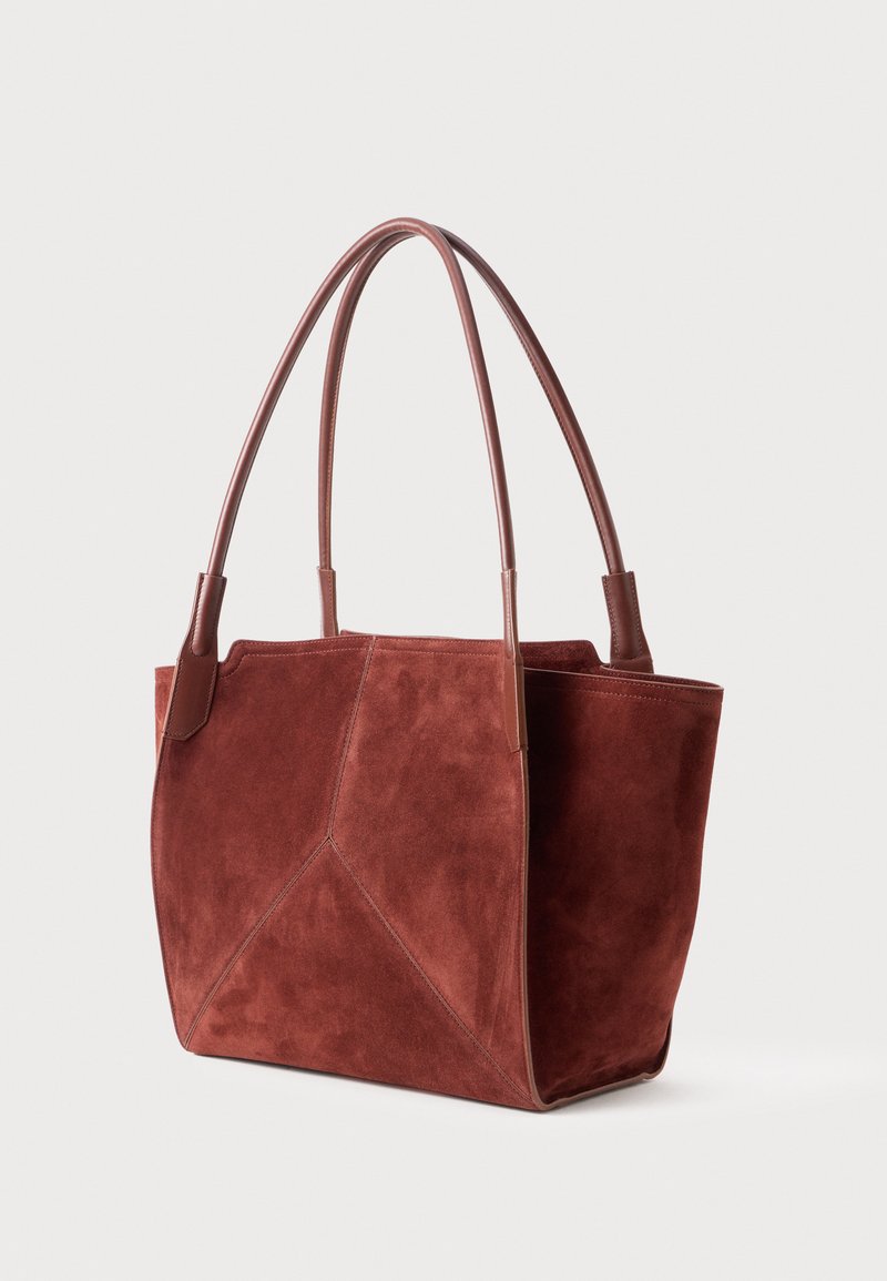 Sac fourre-tout en daim brun avec double poignées en cuir et des détails de couture géométriques, sur fond clair uni.