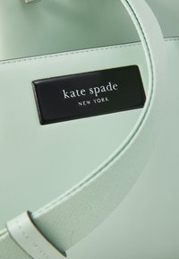 Borsa a tracolla in pelle verde menta con superficie testurizzata, dotata di una toppa logo rettangolare nera con la scritta "kate spade NEW YORK."