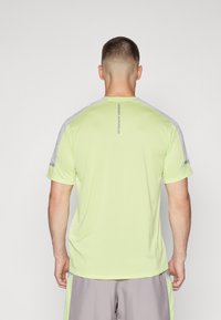 Jasnozielona sportowa koszulka z szarymi akcentami na ramionach. Ma krótkie rękawy i okrągły dekolt, wykonana z lekkiego materiału.