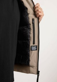 Veste beige avec doublure intérieure noire isolante. Comprend des poches zippées, une étiquette cousue sur le côté et une texture extérieure lisse.