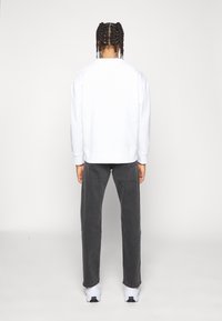 Sudadera blanca con puños y dobladillo acanalados, combinada con pantalones grises y zapatillas blancas. El modelo está de espaldas a la cámara.