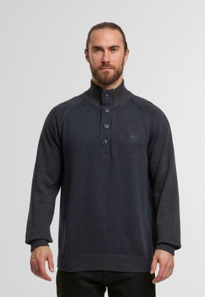 Maglione grigio scuro da uomo con colletto alto a coste, pattina con bottoni e tessuto testurizzato. Le maniche lunghe e i polsini a coste aggiungono dettagli.