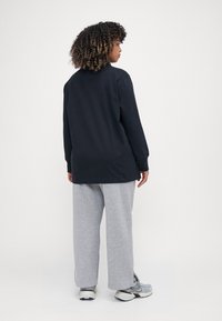 Μαύρη μπλούζα με μακριά μανίκια, χαλαρή εφαρμογή, συνδυασμένη με ανοιχτό γκρι φόρμες. Το ύφασμα φαίνεται μαλακό με λεία υφή και μίνιμαλ σχέδιο.