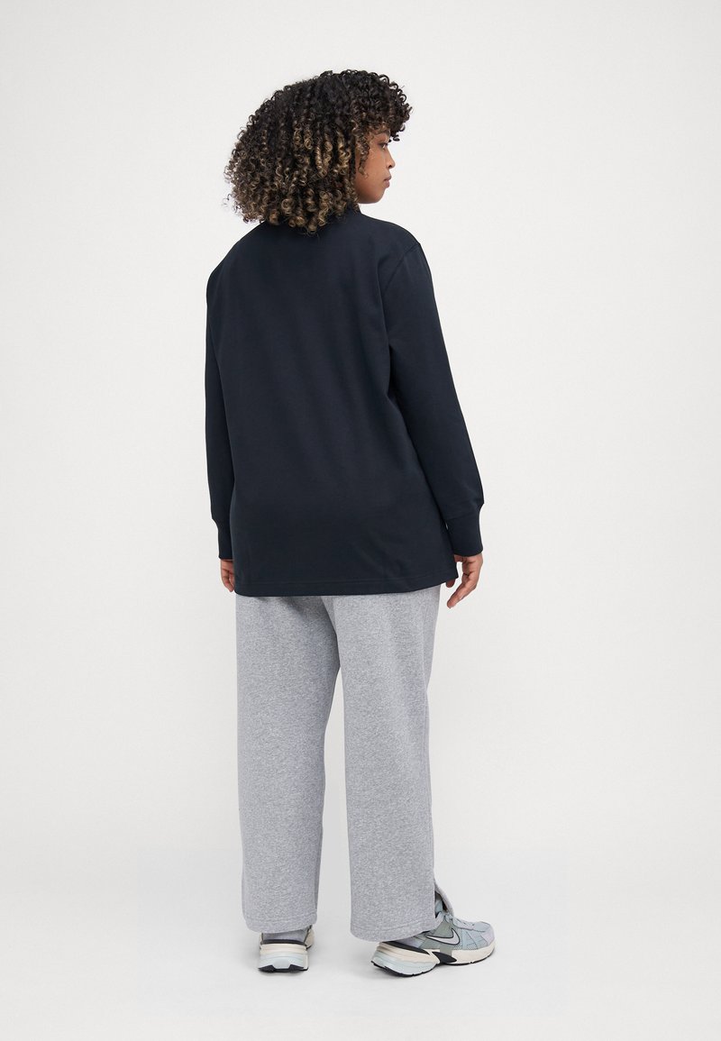 Chemise noire à manches longues, coupe décontractée, associée à un pantalon de survêtement gris clair. Le tissu a l'air doux avec une texture lisse, design minimaliste.