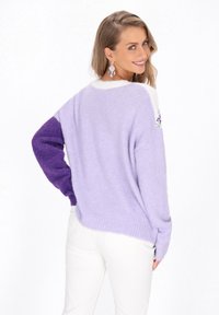 Lila und purpurfarbener gestrickter Pullover mit langen Ärmeln. Verfügt über einen Rippenbund, einen weißen Kragen und lila Akzente an einem Ärmel. Weicher Stoff.