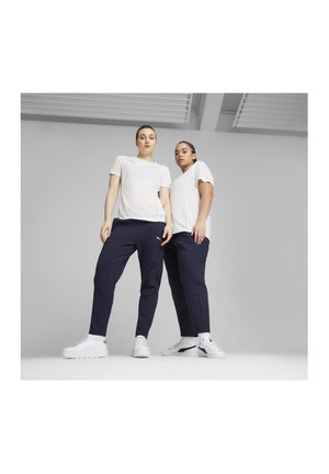 Twee modellen dragen witte t-shirts en marineblauwe joggingsbroeken met witte sneakers. De joggingsbroeken hebben een slim fit en zijnaad.