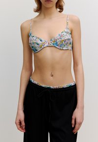 Bloemenprint bralette in pasteltinten met dunne bandjes. Gecombineerd met zwarte broek met trekkoord en een bijpassende bloemenband.