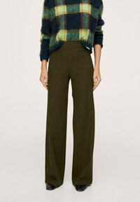 Szerokie spodnie w kolorze oliwkowej zieleni z przednimi kieszeniami. Połączone z wzorzystym, granatowo-zielono-żółtym swetrem z dzianiny. Gładka faktura tkaniny.