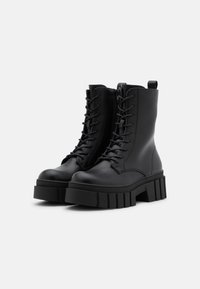 Black leather ankle boots with a high, chunky platform sole, rounded toe, and front lacing. Features a pull tab at the back for easy wear.