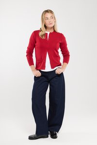 Czerwony sweter z dzianiny, okrągły dekolt, zapięcie na guziki z przodu i prążkowane akcenty, w połączeniu z luźnymi ciemnymi dżinsami i czarnymi butami.