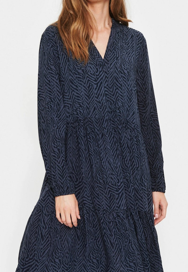 Robe bleu marine à manches longues avec un col en V, un motif en zigzag texturé et un ourlet à volants. Comprend des poignets froncés et une coupe décontractée.