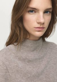 Pull à col montant marron clair en matière douce et texturée, présentant un design simple sans ornements.