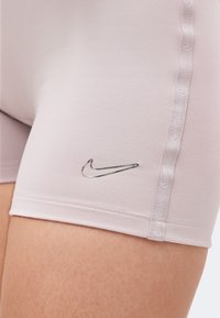 Κοντινή λήψη ανοιχτόροζ αθλητικών σορτς με ασημένιο λογότυπο Nike και ραμμένη πλαϊνή τρέσα στο επάνω μέρος του μηρού ενός ατόμου.