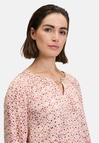 Blusa a maniche lunghe di colore rosa con motivi circolari. Tessuto morbido, scollatura a chiave con un accento metallico. Texture sottile e vestibilità rilassata.