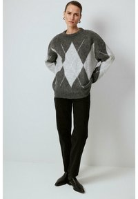 Szürke és fehér argyle mintás, oversized pulóver, puha anyagból készült, fekete kordbársony nadrággal és bokapuszta csizmával párosítva.