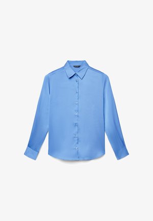 Chemise à manches longues bleu clair avec boutons, col pointu et poignets, posée à plat sur un fond blanc.
