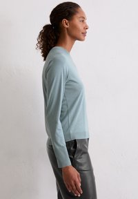 lichtblauw, lang mouwtop van zacht materiaal, met ribbelmanchetten en -zoom, gecombineerd met zwarte leren broek.