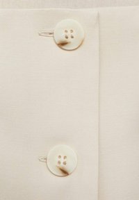 Tissu beige avec une texture lisse présentant deux boutons de couleur crème. Chaque bouton possède quatre trous pour la fixation.