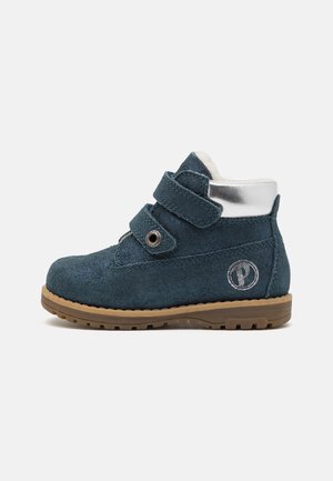 Bottine en daim bleu foncé pour enfants avec deux bandes auto-agrippantes, semelle en caoutchouc marron et détail argenté au talon et sur le logo latéral.
