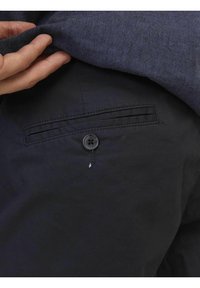 Pantaloni in tessuto nero con tasca posteriore, cuciture dettagliate e chiusura a bottone scuro, che mostrano la texture e la morbidezza del materiale.