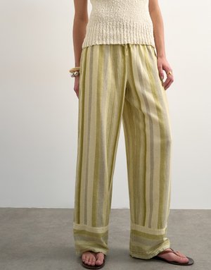 Person iført løse, vide bukser med vertikale grønne og beige striper, kombinert med mørke flip-flops og en ermeløs strikket topp.