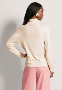 Crème col roulé trui met geribbelde manchetten en zoom, gecombineerd met roze wijde broek. Gladde brei textuur, aansluitende silhouet, minimalistisch ontwerp.