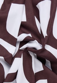 Tessuto intrecciato con un grande motivo astratto in marrone e bianco. La texture è liscia, con una qualità leggera e drappeggiante.